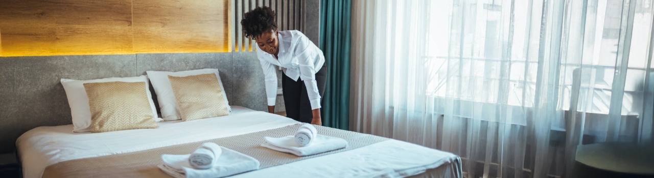 A cleaner is making a bed in a hotel room.